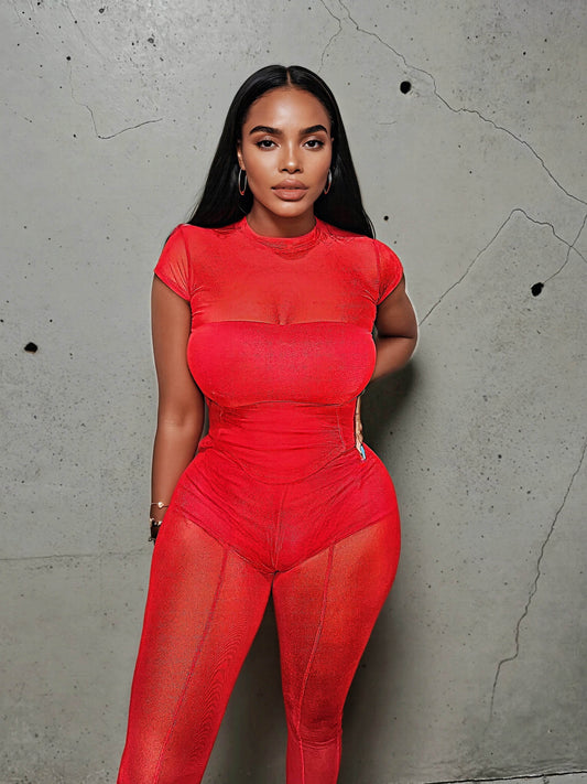 Model poses confidently in a fitted carnelian red mesh three piece set featuring a sheer cap short sleeve top and high-waisted leggings with built-in contour paneling. The bold color and body-hugging fit highlight a confident, fashion-forward silhouette against a raw concrete backdrop.